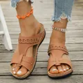 Close-up of tan wedge sandals with laser-cut detailing and contrast stitching on wood - Tan