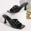 Macro view of crocodile texture and gold hardware on black square-toe heel sandals. - Black