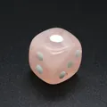 Primer plano detallado de un dado de piedra natural rosa con puntos sobre fondo negro - Cuarzo rosa