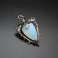 Macro view of vintage bronze heart pendant featuring a teardrop opal stone and ornate metalwork - Opal