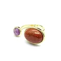 Gros plan d'une bague rétro en or avec une pierre goldstone ovale et un cristal violet rond. - Pierre de Sable d'Or