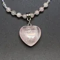 Close-up detail of a delicate pink natural stone heart pendant on a beaded necklace chain. - Rose Quartz