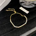 Detailansicht eines goldenen verstellbaren Armbands mit glitzernden Steinen - Weiß