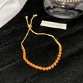 Nahaufnahme eines verstellbaren goldfarbenen Armbands mit leuchtend orangen Steinen. - Orange