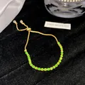 Detailansicht eines eleganten Goldarmbands mit grünen Kristallen auf schwarzem Samt. - Strass Schiebearmband / Grün