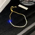 Detailaufnahme eines verstellbaren vergoldeten Armbands mit bunten schillernden Kristallen - Feines Blassbläuliches Weiß