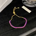 Detailansicht eines verstellbaren goldfarbenen Armbands mit leuchtend lila Zirkonia-Steinen. - Lila