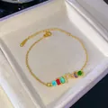 Pulsera dorada con letra F de pedrería arcoíris en caja de joyería blanca - Letra F