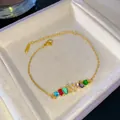 Elegante pulsera dorada con piedras preciosas de colores y una letra K de cristal - Letra K