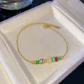 Elegante pulsera dorada con gemas de colores y detalle de amuleto de letra O de cristal. - Letra O