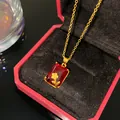 Detalle de collar dorado con gema roja rectangular y rosa tallada en estuche de joyería - Rosa Piedra Roja Rectangular