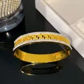Close-up detail of gold titanium steel bracelet featuring Greek key pattern and crystals. - Greek Key Rhinestone Bangle / Gold