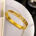 Close-up of gold titanium steel bangle with hollow Greek key and four-leaf clover motifs. - Pave Rhinestone Hollow Meander Clover / Gold