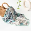 Foulard quadrato in seta premium con elegante stampa floreale blu drappeggiato su un cesto - grigio-blu