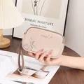 Detailed view of beige double zipper clutch with colorful leaf print and gold bird emblem - Apricot