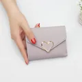Mauve faux leather mini folding wallet featuring a gold heart buckle design held by hand - Heart Style / Light Purple
