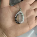Primer plano de un colgante guardapelo plateado con forma de lágrima en una mano - Estilo Liso