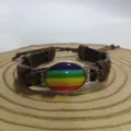 Detailansicht eines handgefertigten Regenbogen-Lederarmbands auf einer Holzscheibe. - Braun