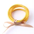 Close-up of golden silicone Buddhist jonc bangles tied with a beige ribbon bow - Antique Gold