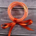 Close-up detail of seven orange glitter silicone jelly bangles tied with a matching satin ribbon - Orange