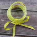 Close-up of neon yellow glitter jelly bangles tied with a matching satin ribbon. - Yellow