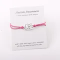 Detailopname van zilveren puzzelarmband met roze koord op Autism Awareness-kaart - Rozerood
