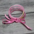 Detalle de pulsera de silicona de cinco capas con cuentas rosas y lazo de satén decorativo. - Rosa