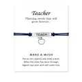 Nahaufnahme des Lehrer-Wunscharmbands mit blauem Band und Apfelanhänger auf Karte - TEACH Buchstaben & Apfel Stil / Marineblau