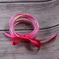Set of seven pink glitter silicone jelly bangles tied with a decorative satin ribbon bow. - Rose Red