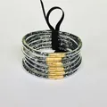 Close-up of 6-layer glitter-filled PVC bangles with gold accents and black ribbon. - Black