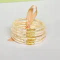 Close-up detail of six-layer glitter-filled silicone bangles tied with a peach ribbon - Champagne