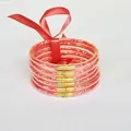 Detail view of 6-layer glitter silicone bracelets with red satin ribbon bow and gold links. - Red