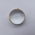 Primer plano de un colgante de caja Gawu de cristal convexo con marco de acero inoxidable dorado - Exterior 45mm Interior 40mm Espesor 12mm / Dorado