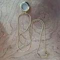 Vue détaillée d'un collier médaillon flottant en acier doré sur une surface en bois naturel - Collier Pendentif (Avec Chaîne Serpent) / 20mm / Or