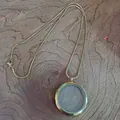 Vue détaillée d'un collier médaillon en acier inoxydable doré sur fond bois. - 38 mm doré avec chaîne serpent