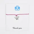 Detail of a pink wax cord bracelet featuring a silver winged tooth charm on a card. - Rose Red