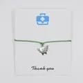 Close-up of winged tooth charm bracelet on white thank you card with green cord. - Green