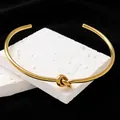 Detailansicht eines minimalistischen vergoldeten Titanstahl-Armreifs mit Knotenmuster auf Stein - Armreif / Gold