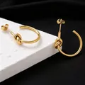 Nahaufnahme goldener Knoten-Creolen aus Titanstahl mit einer polierten Oberfläche - Ohrringe / Gold