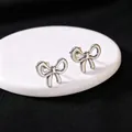 Close-up van minimalistische zilveren strik oorknopjes op een witte displaystandaard - Stud oorbellen / Staalkleur