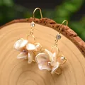 Nahaufnahme eleganter handgefertigter Barockperlen-Blumenohrringe auf Holzsockel - 3D Blumen Ohrringe