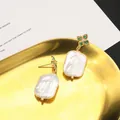 Elegant baroque pearl earrings with green clover stud design on a golden tray - White Emerald Clover Studs