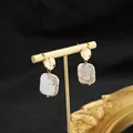 Elegant Baroque pearl earrings with hammered gold-tone studs on a display stand. - White Irregular Groove Studs