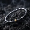Detailreiche Makroaufnahme eines schwarzen Metallperlenarmbands mit goldenem Kreuz - Goldenes Kreuz-Stil (S1345-B) / Dunkelgraues Armband