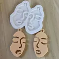 Detailed view of an abstract face silicone mold and two finished beige resin keychains - L