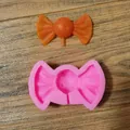 Detailansicht einer rosa Silikonform für Schleifen-Lollipops und einer orangefarbenen Süßigkeit - Schleife