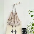 Detailed view of large floral print canvas tote bag hanging on a minimalist white wall hook - Ink Stone Texture