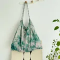 Detailed view of large tie-dye canvas tote bag hanging on a hook with rope straps - Emerald Green Ink Painting