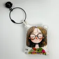 Detail view of a cartoon girl canvas bag charm with black bell and metal wire ring. - LOVE Text Girl