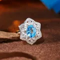 Close-up of S925 sterling silver ring featuring a vibrant oval blue topaz and floral halo. - Natural Swiss Blue Topaz / Blue